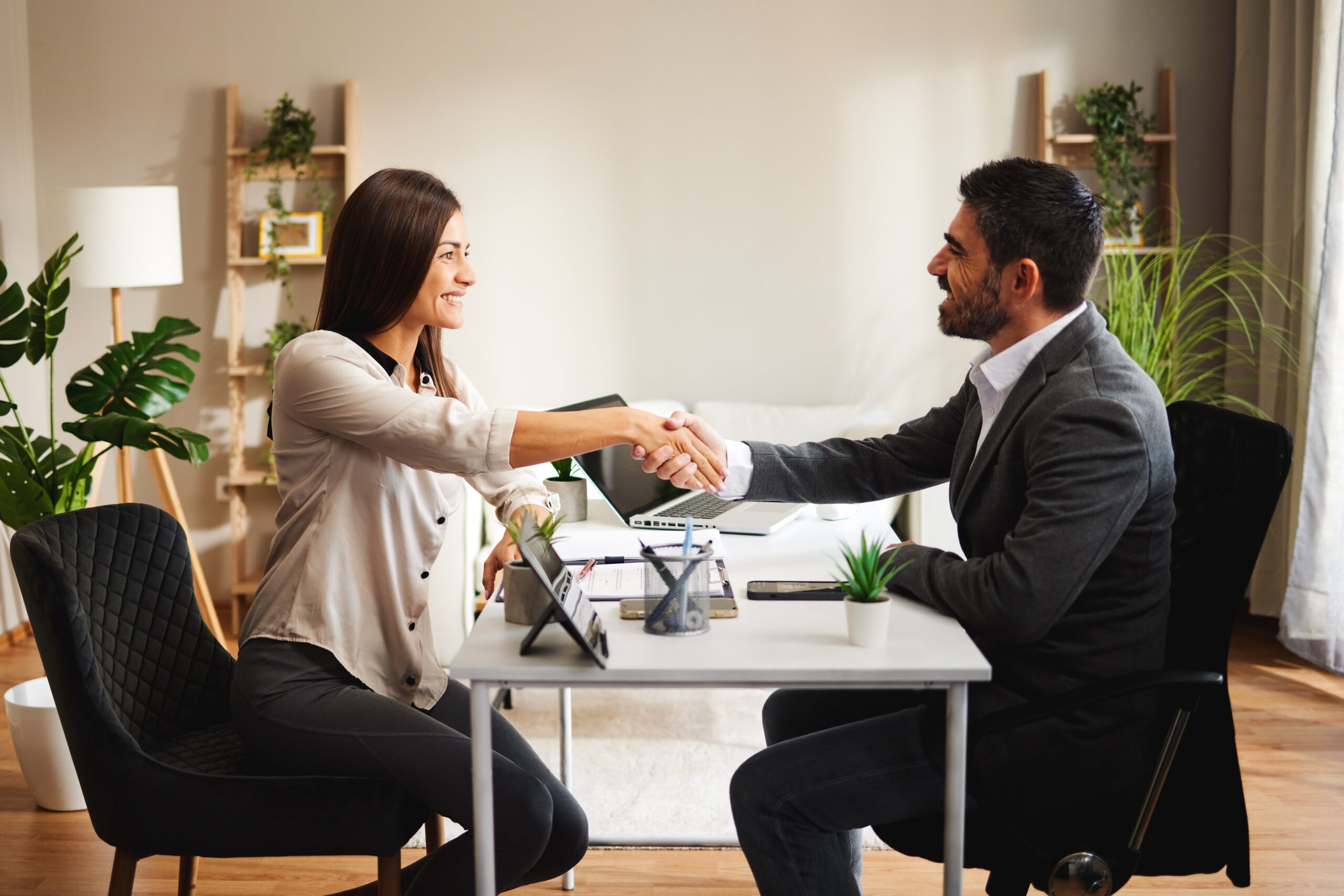 shutterstock_2218220009 Two people shaking hands in an office, with text boxes displaying a conversation about completing and checking a bookkeeping setup.
